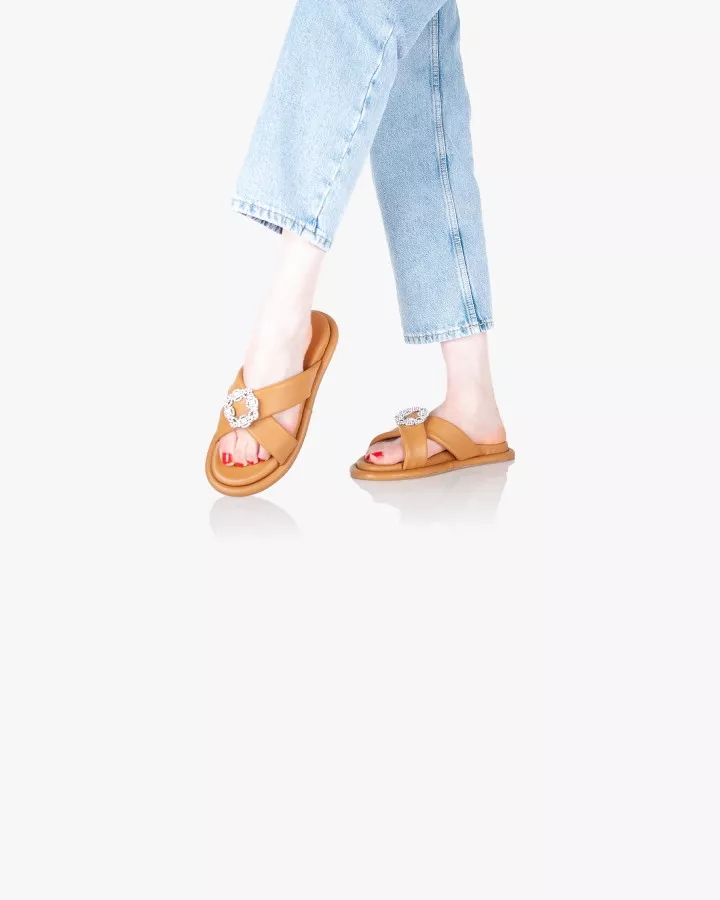 Sandales en cuir camel avec accessoires bijoux portées debout jambes croisées pied gauche levé